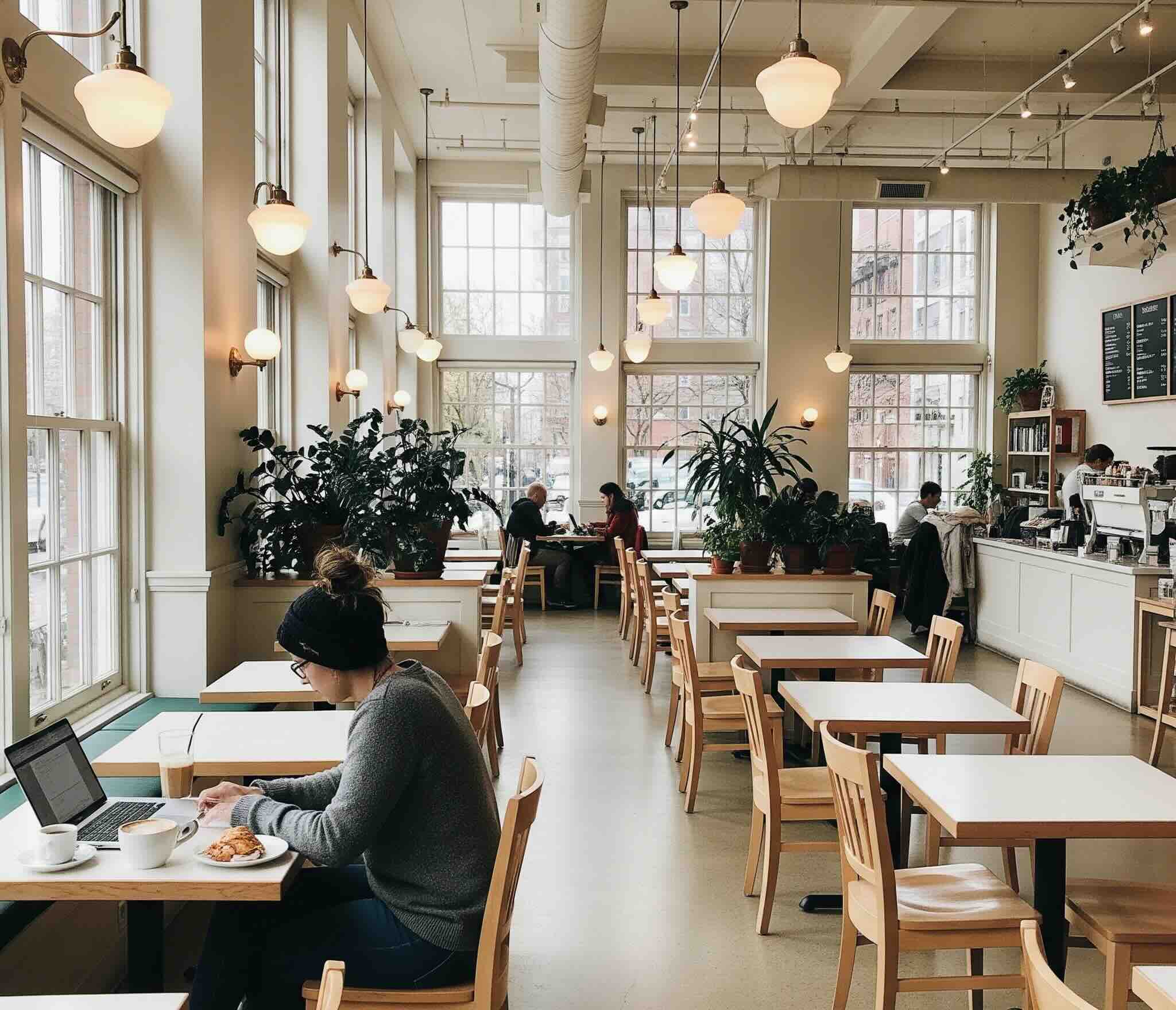 A bright and airy Hillcrest coffee shop with wooden tables, lush plants, and guests working on laptops by large windows